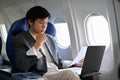 Successful Asian businessman checking his paperwork, using laptop during the flight Royalty Free Stock Photo