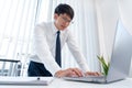 Successful Asian Businessman with glasses Working on Laptop analyzing data sitting at his desk in bright office space getting the Royalty Free Stock Photo