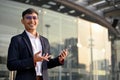 Successful Asian businessman holding his smartphone and standing on a city street Royalty Free Stock Photo