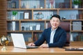 Successful asian businessman looking at camera and smiling, man working in classic office at desk, with laptop, looking at camera Royalty Free Stock Photo