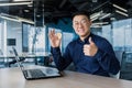 Successful asian businessman smiling and looking at camera, holding bitcoin coin and giving thumbs up, man working Royalty Free Stock Photo