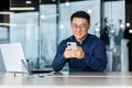 Successful Asian businessman working inside modern office building, man smiling and happy using smartphone to browse Royalty Free Stock Photo