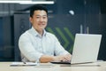 Successful asian businessman working in modern office with laptop typing, smiling and looking at camera Royalty Free Stock Photo