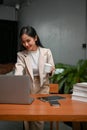 Successful Asian businesswoman looking at laptop screen, holding a coffee cup Royalty Free Stock Photo