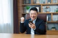 Successful Asian uses a smartphone, businessman looks at the phone screen, and rejoices and smiles celebrates victory, rejoices at