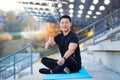 Successful athlete sitting in lotus position in the morning meditating, asian man looking at camera and smiling holding thumbs up Royalty Free Stock Photo