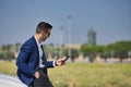 Successful, attractive, young Hispanic man in jacket and sunglasses consulting his cell phone leaning on the hood of his white Royalty Free Stock Photo