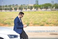 Successful, attractive, young Hispanic man in jacket and sunglasses consulting his cell phone leaning on the hood of his white Royalty Free Stock Photo