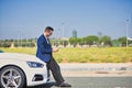 Successful, attractive, young Hispanic man in jacket and sunglasses consulting his cell phone leaning on the hood of his white Royalty Free Stock Photo