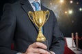 Successful awarded businessman is holding golden trophy. Lights and flashes in background