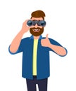 Successful bearded man in casual wear looking through binoculars & gesturing, making thumbs up sign with hand finger.