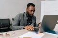 Successful black male businessman sitting at worktable at modern office, typing on computer keyboard, sending emails to Royalty Free Stock Photo