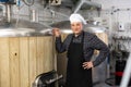 Successful brewer standing in brewery near fermentation tanks