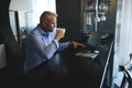 Successful business man in business casual attire drinking coffee in the morning, sitting at a table with laptop and digital Royalty Free Stock Photo