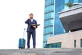 Successful business man stands on the steps against the background of an office building with documents in his hands Royalty Free Stock Photo