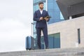 Successful business man stands on the steps against the background of an office building with a project business documents in his Royalty Free Stock Photo