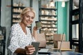 Successful business owner. Beautiful and happy business woman drinking coffee, using smartphone and smiling while