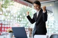 Successful business woman celebrating her achievement with arms up in front of laptop computer at office desk Royalty Free Stock Photo