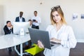 Successful business woman standing with laptop with her staff in background at modern bright office Royalty Free Stock Photo