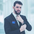 Successful businessman adjusting his necktie while standing near a window in bright office. Royalty Free Stock Photo