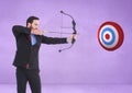 Successful businessman aiming target with bow and arrow against purple background