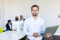 Successful businessman with laptop smiling at camera while her colleagues standing behind him in office Royalty Free Stock Photo