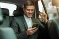 Successful businessman making online payment using bank card while riding on back seat of car on way to meetting with partners, Royalty Free Stock Photo