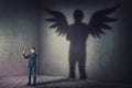 Successful businessman, raising hands up, celebrating victory, casting a superhero shadow with angel wings on a dark room wall.