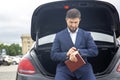 Successful businessman sits with a diary on the hood of his prestigious car