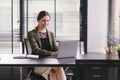 Successful businesswoman in a stylish dress is sitting at a desk in a modern office, using a laptop computer. She Royalty Free Stock Photo