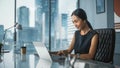 Successful Businesswoman in Stylish Dress Sitting at a Desk in Modern Office, Using Laptop Computer Royalty Free Stock Photo