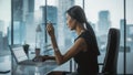 Successful Businesswoman in Stylish Dress Sitting at a Desk in Modern Office, Using Laptop Computer Royalty Free Stock Photo