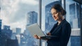 Successful Businesswoman in Stylish Dress Working on Laptop, Standing Next to Window in Big City Royalty Free Stock Photo