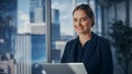 Successful Businesswoman in Stylish Dress Working on Laptop, Standing Next to Window in Big City Royalty Free Stock Photo