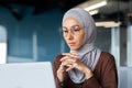 Successful businesswoman thinking at workplace, muslim woman in hijab using laptop at work, serious arab woman sitting