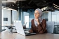 Successful businesswoman thinking at workplace, muslim woman in hijab using laptop at work, serious arab woman sitting