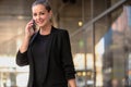Beautiful modern business woman entrepreneur on cellphone smiling with success in black stylish suit in business district