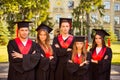 Successful confident five graduates in robes and hats standing in row while crossing hands