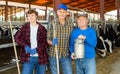Successful elderly dairy farm owner with son and teen grandson standing in stall with cows