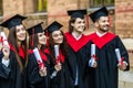 Successful excited five graduates in robes standing in row and showing certificate