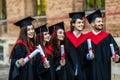 Successful excited five graduates in robes standing in row and showing certificate