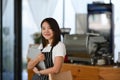 A female entrepreneur wearing black apron hands holding tablet and standing in her own coffee shop.