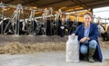 Female farmer posing with can of milk near stall with cows