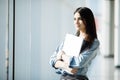 Successful female office worker with laptop is standing in skyscraper interior against big window with city view on background. Royalty Free Stock Photo