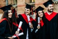 Successful excited five graduates in robes standing in row and showing certificate