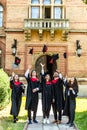 Successful five students with congratulations together throwing graduation hats in the air and celebrating at University