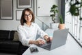 Successful freelancer. Happy lady sitting at desk with laptop and smiling at camera, working on computer in cozy office Royalty Free Stock Photo