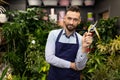 successful gardener florist stands in a flower shop with a pruner in his hands and looks with a smile at the camera