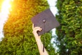 Successful graduate, in academic dresses, raised up graduation c
