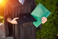 Successful graduate guy, in academic dresses, on graduation posing, holding a green folder and looking at it, farewell study, can